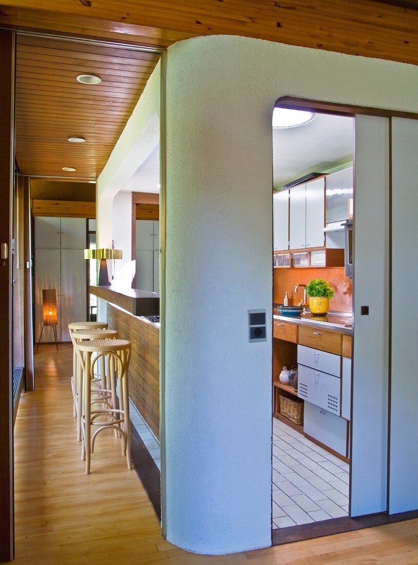 Kücheneinbau mit abgerundeter Ecke und offene Schiebetür mit Blick auf Küchenzeile, an der Seite Durchreiche und Thonet Barhocker