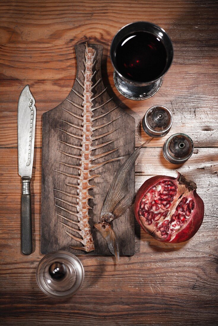 A still life featuring a fish skeleton, pomegranate and red wine