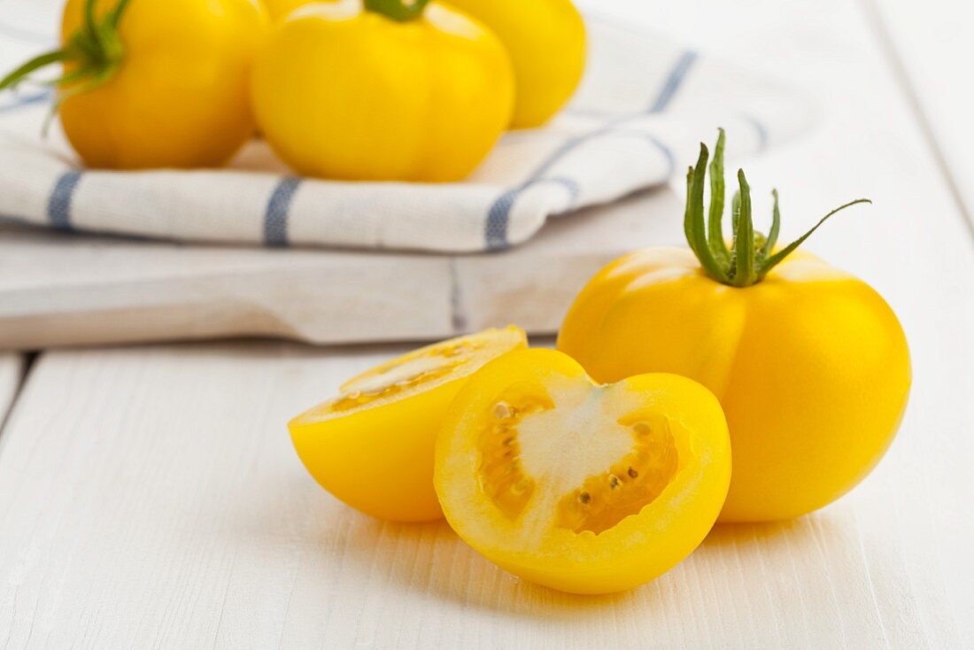 Gelbe Tomaten (Sorte Goldene Königin), ganz und halbiert auf weißem Küchentisch