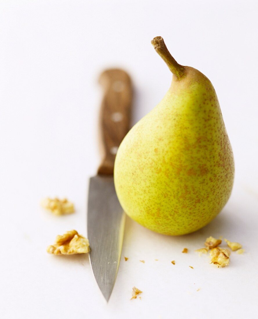 A pear with a knife and pieces of walnut