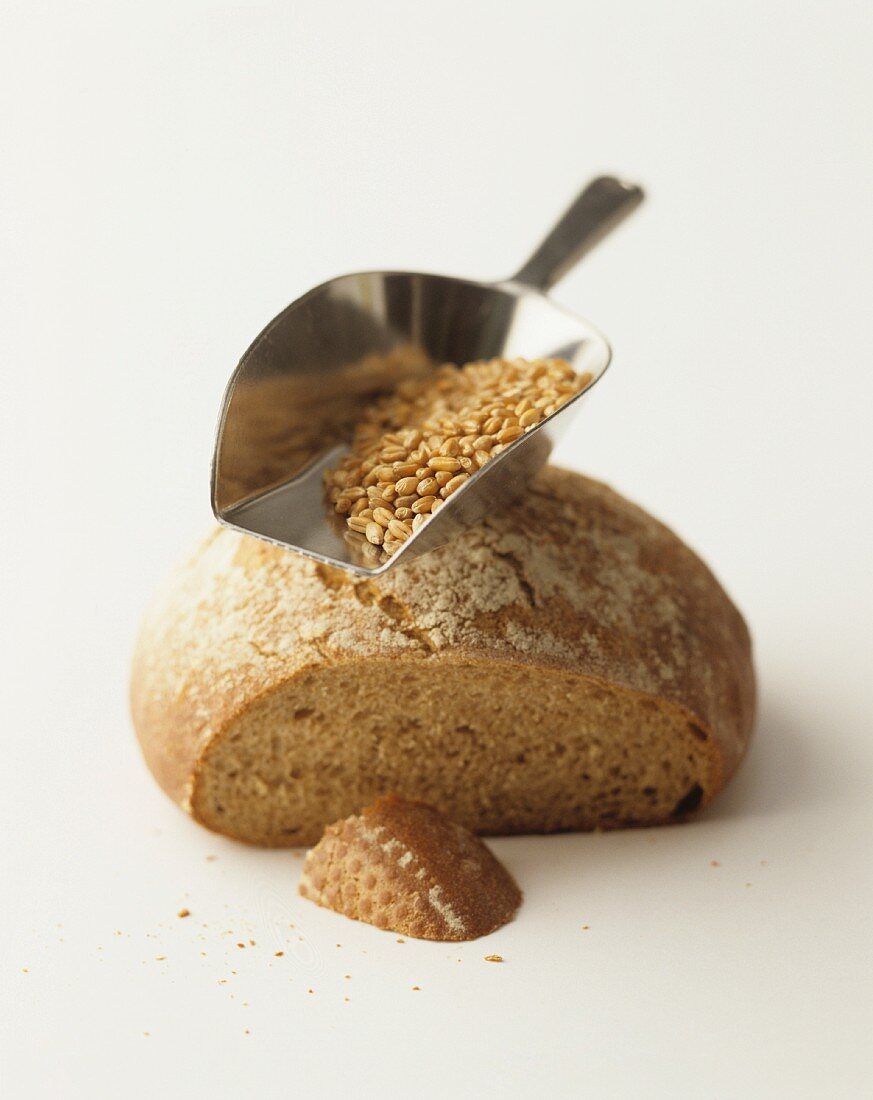 A partly sliced loaf of bread, and a scoop of cereal grains