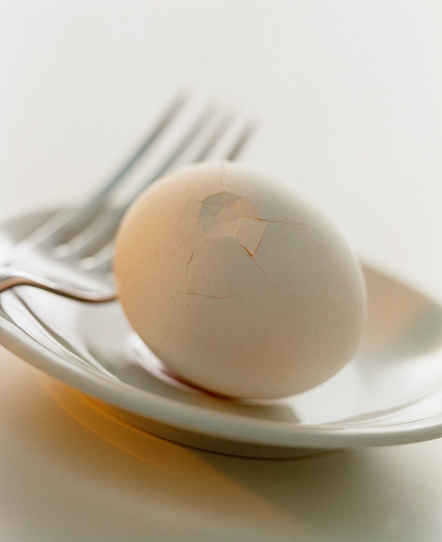 A white hen's egg with crushed shell on a plate
