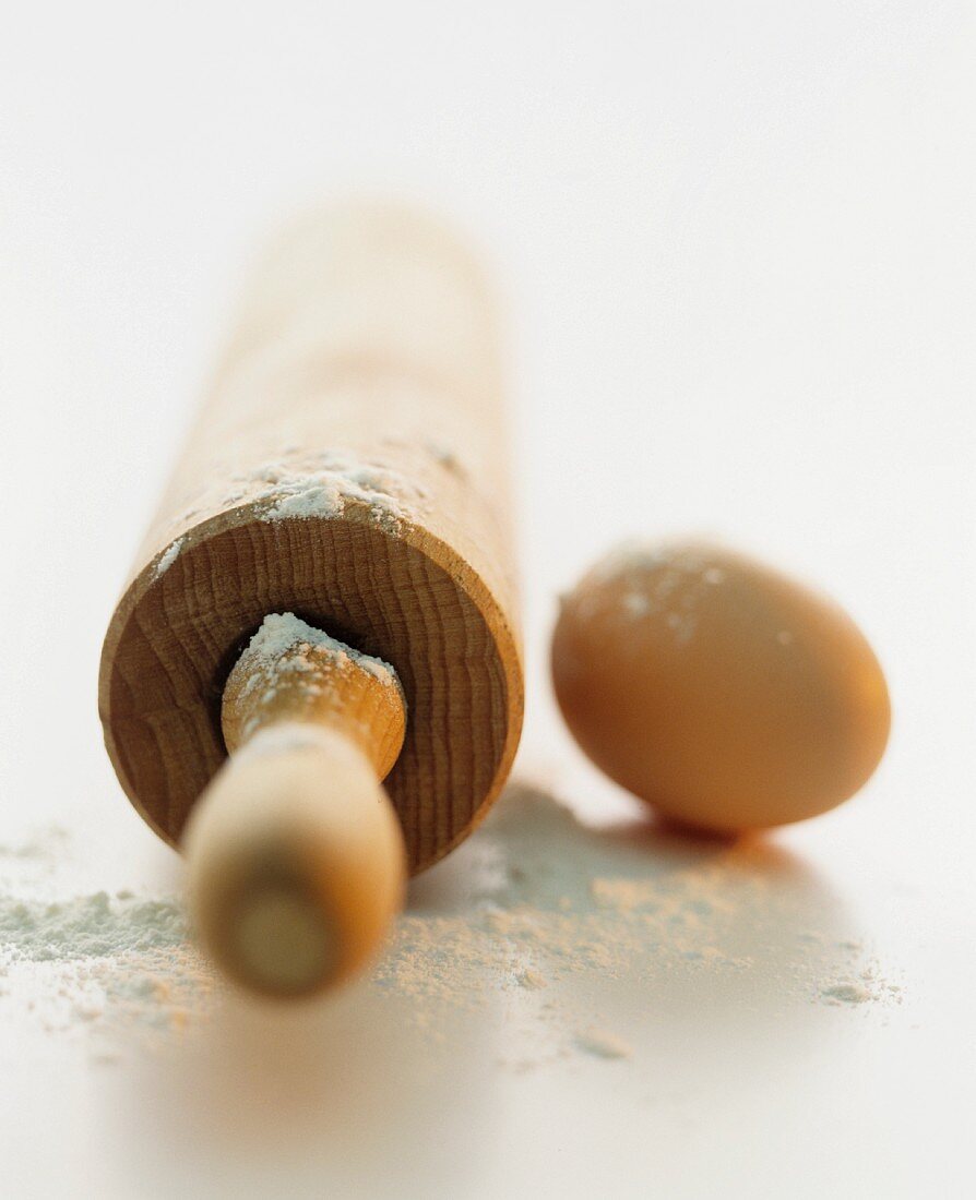 A still life featuring a rolling pin, flour and an egg