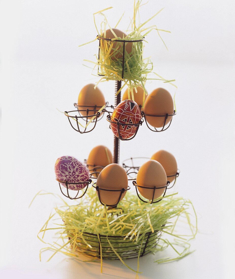 Brown hen's eggs and painted eggs with hay in an egg holder