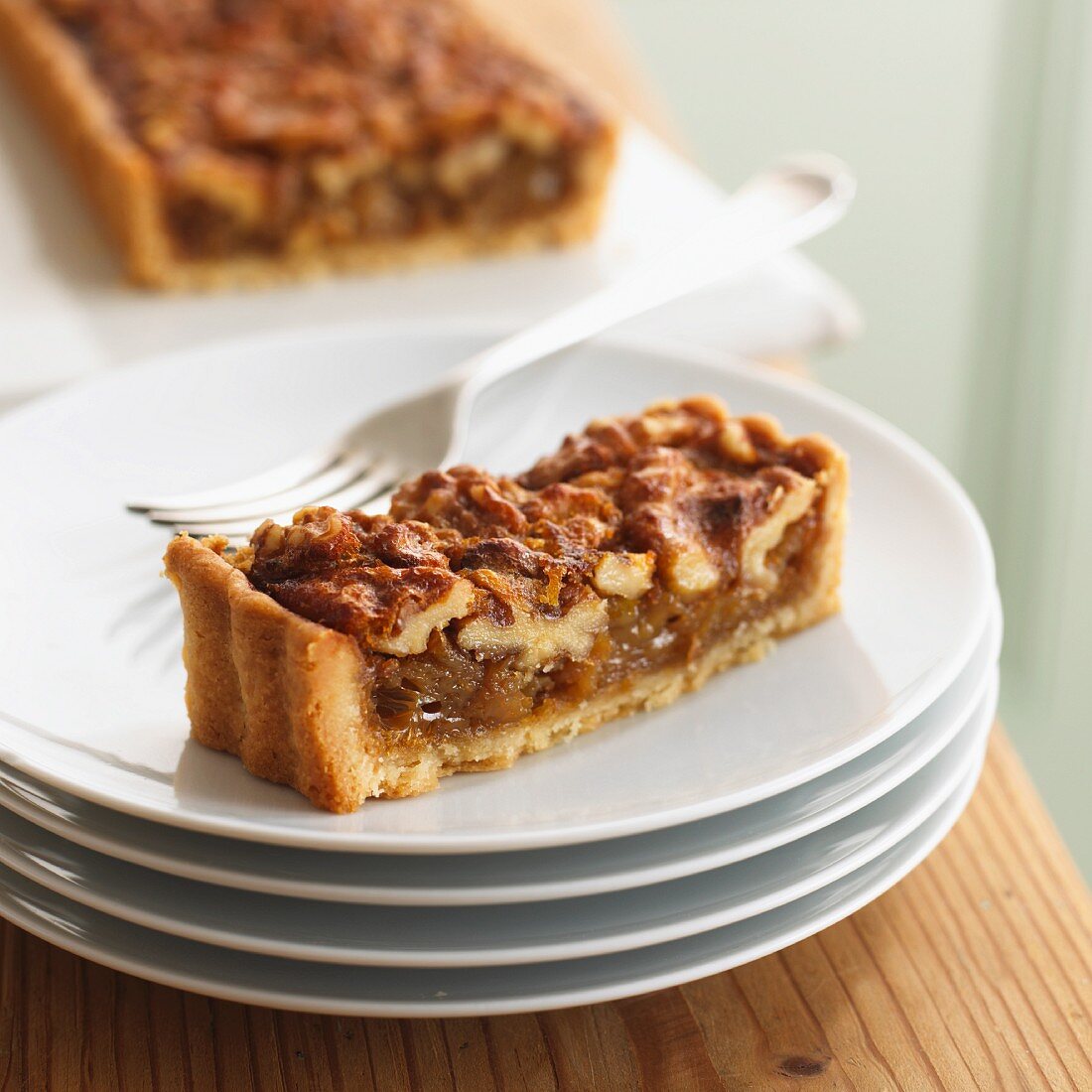 A piece of walnut tart in front of a sliced walnut tart