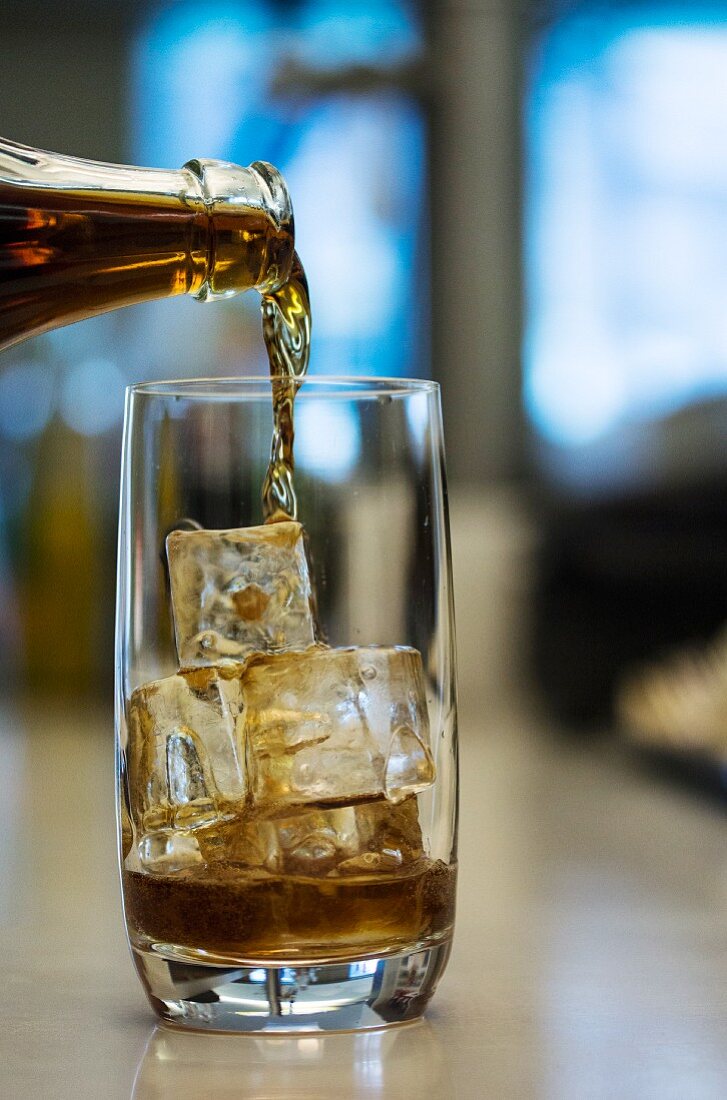 A cola drink being poured into a glass with ice cubes