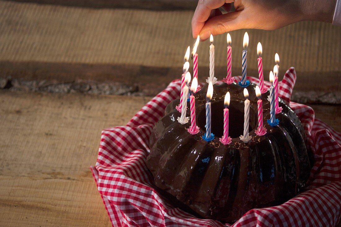 Candles being lit on top of a chocolate Bundt cake