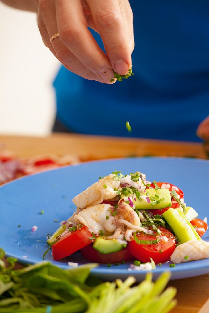 Schnittlauch auf Tomaten-Gurken-Salat mit Tintenfisch streuen