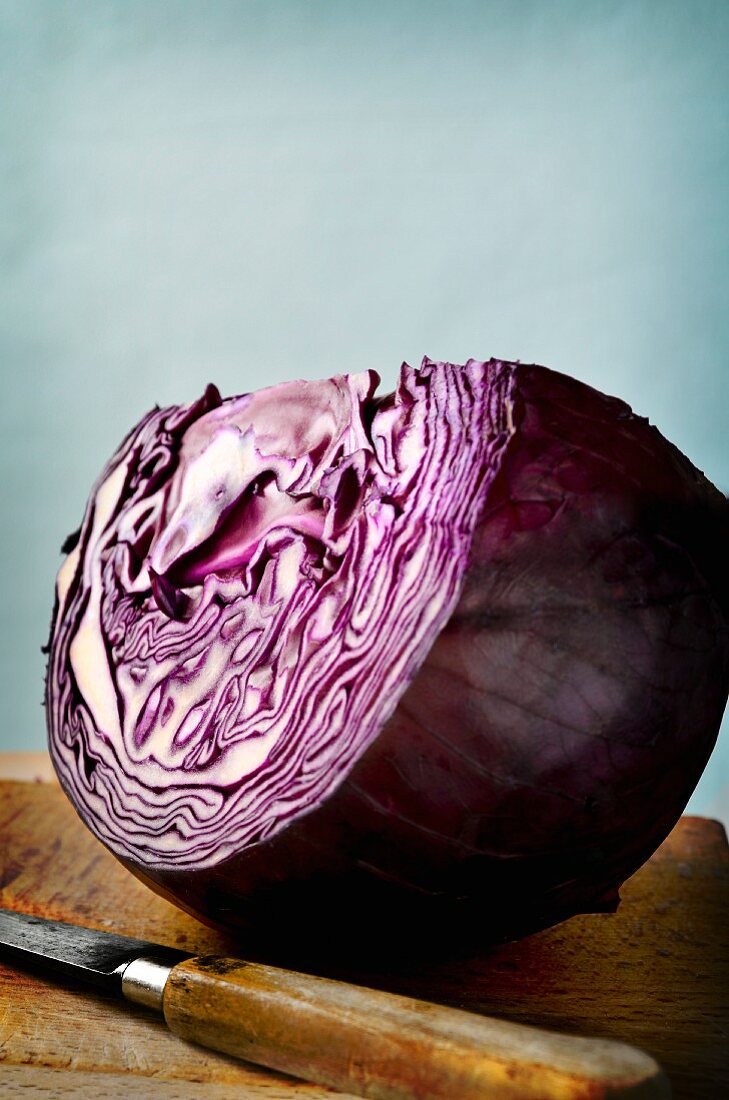 A large wedge of red cabbage on a wooden board with a knife