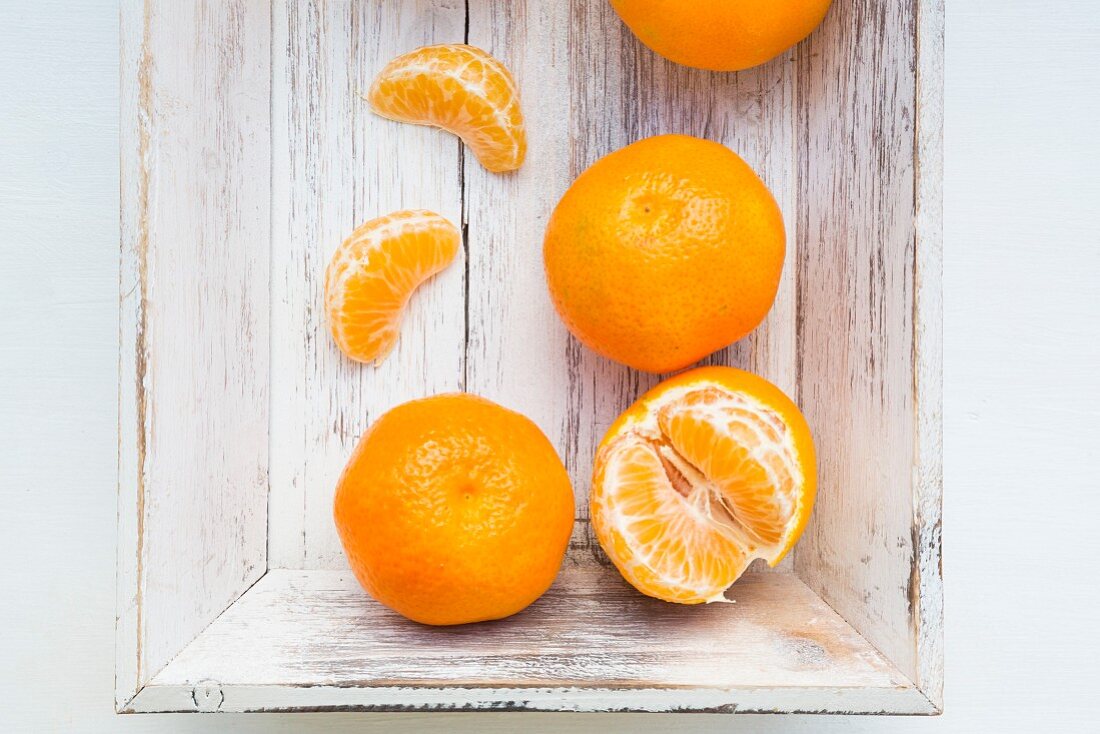 Clementine oranges, whole and peeled, on a wooden tray