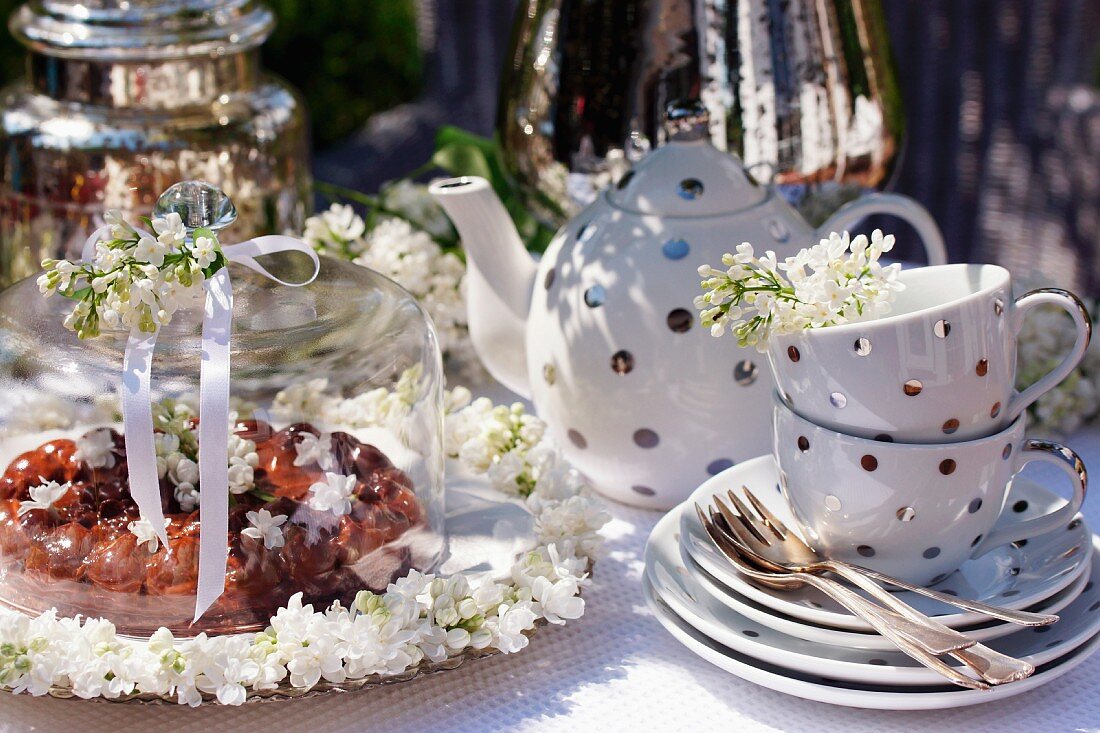 Schokoladenkuchen, weisser Flieder und Teegeschirr auf Gartentisch