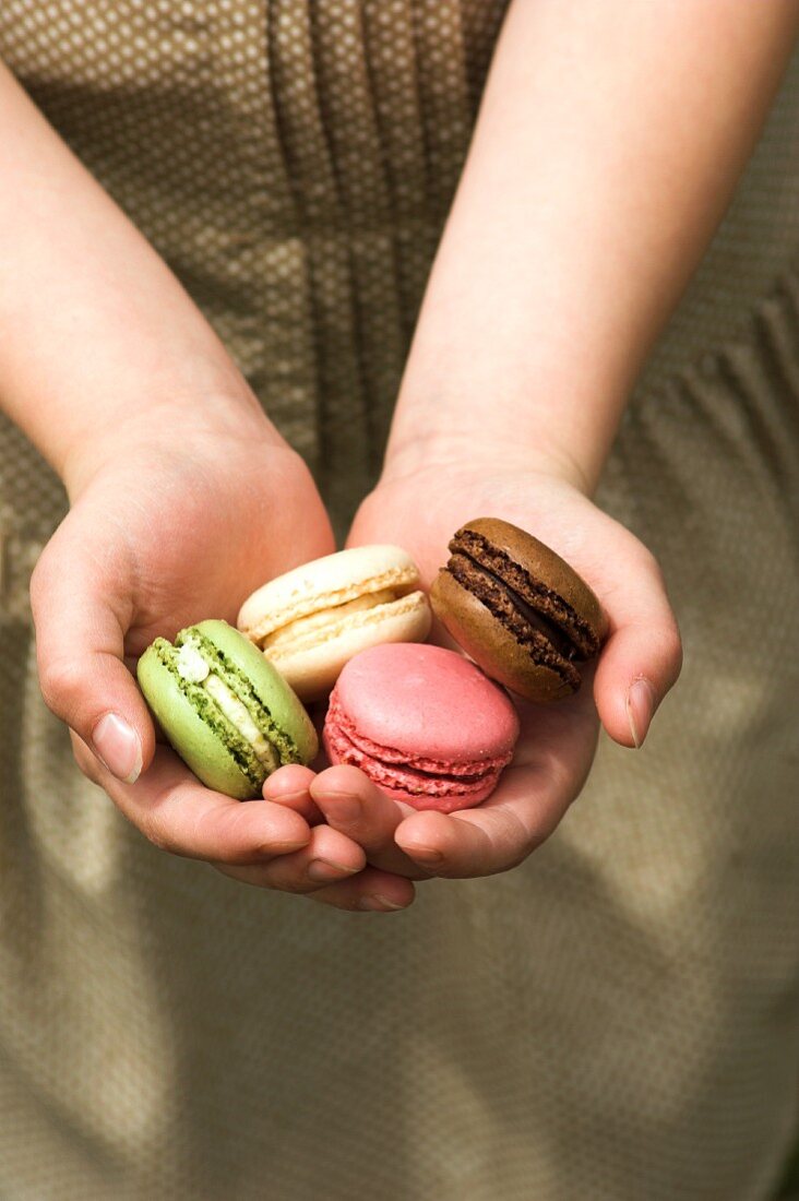 Hands holding four macarons