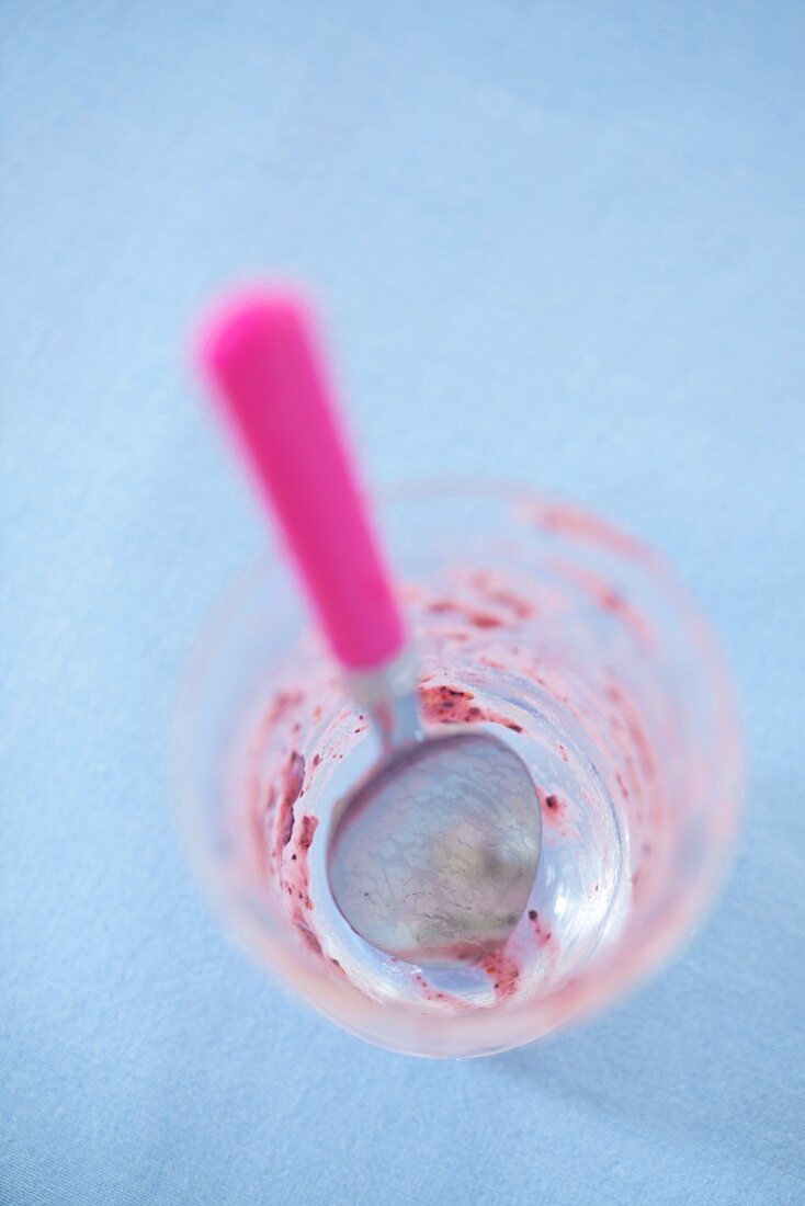 The remains of raspberry ice cream in a glass with a spoon