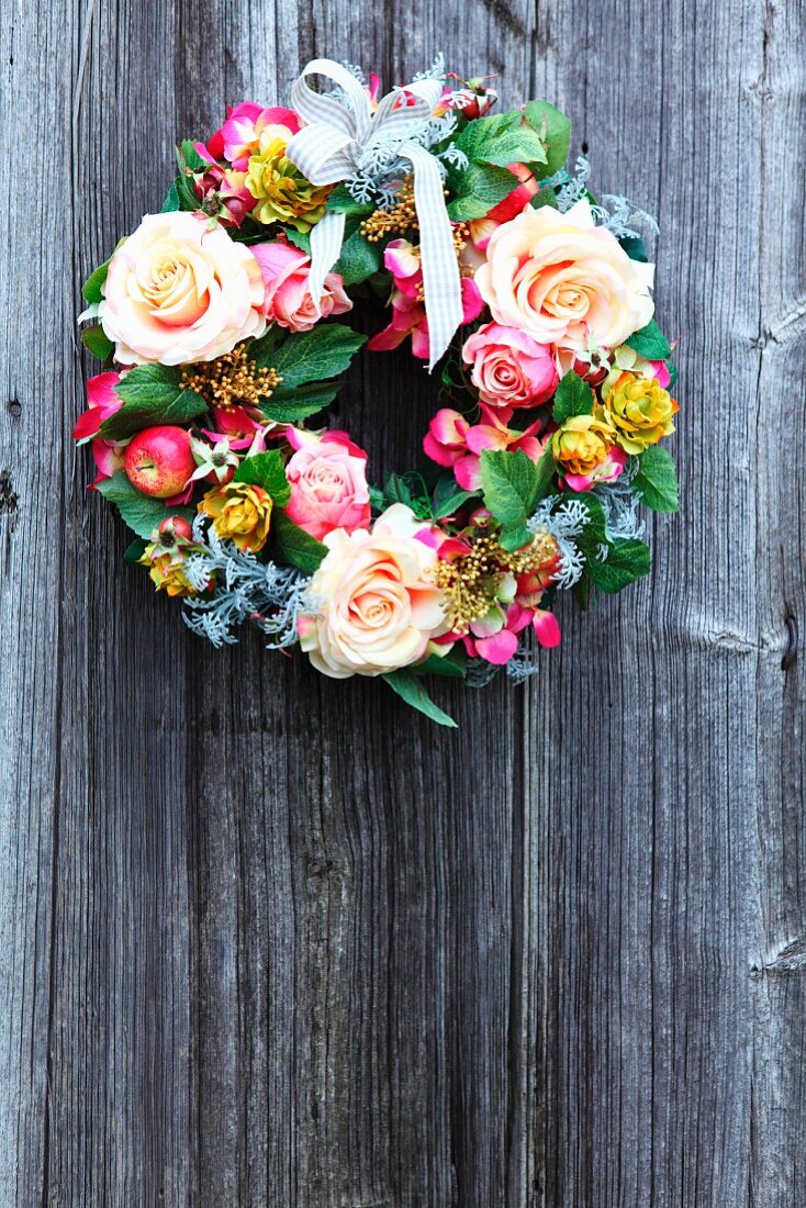 Dekokranz mit verschiedenen Blumenblüten und Schleife an Holzwand