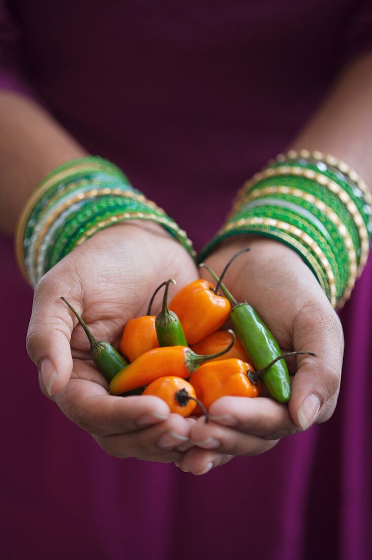 Hands Holding Green and Orange Chili Peppers