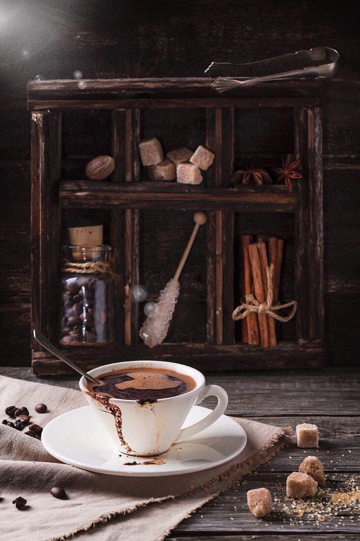 Cup of coffee served on old wooden table with sugar and spices