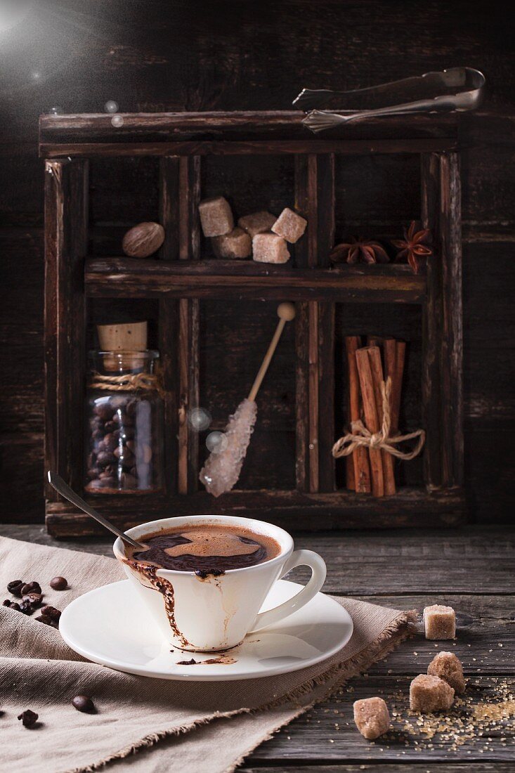 Eine Tasse Kaffee auf einem alten Holztisch mit Zucker und Gewürzen