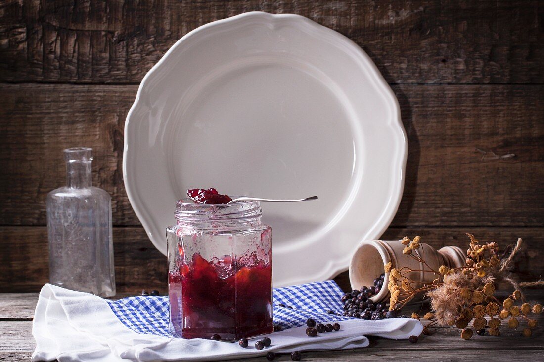 Jar of plum and juniper jam on old wooden background