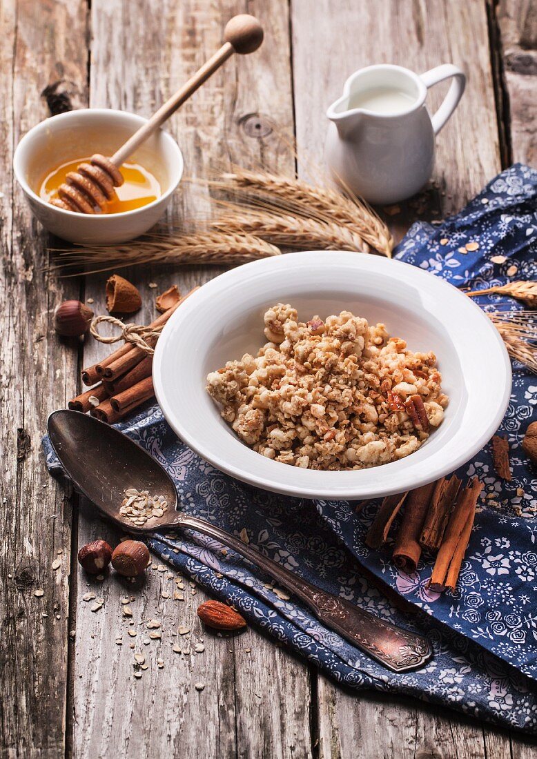 Teller mit Müsli, Milch, Honig, Zimt und Nüsse auf rustikalem Holztisch