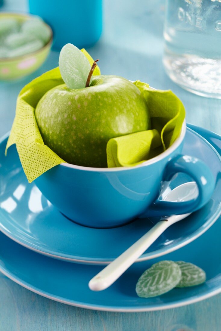 Green apple in blue cup and leaf-shaped sweets on plate