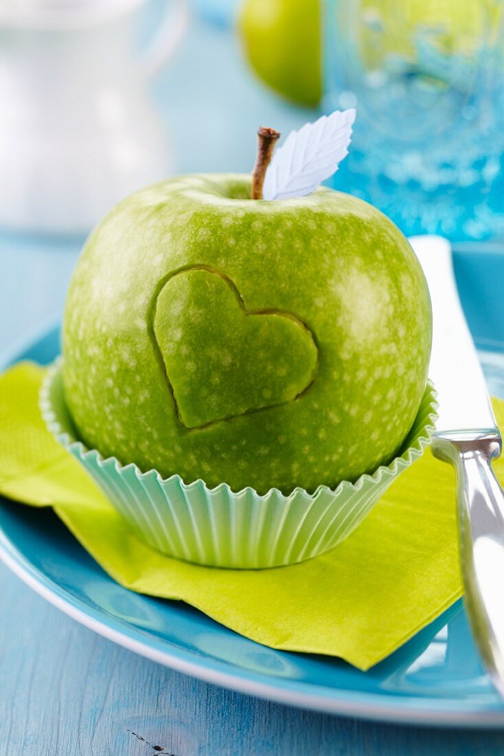 Green apple carved with love heart in cake case on plate