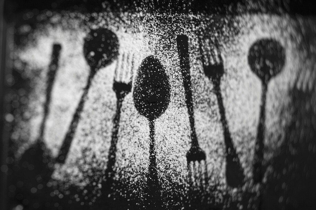 The outlines of forks and spoons in icing sugar on a dark surface