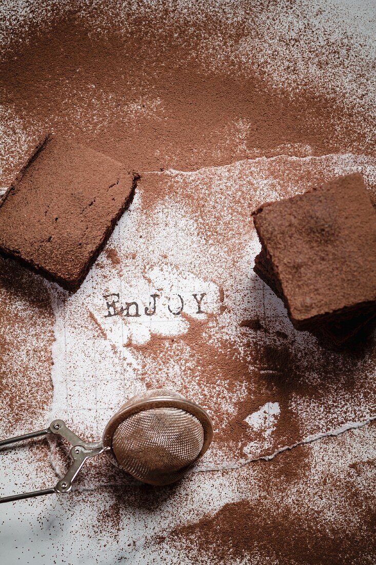 Drei kakaobestäubte Brownies auf weißem Zettel mit der Aufschrift Enjoy