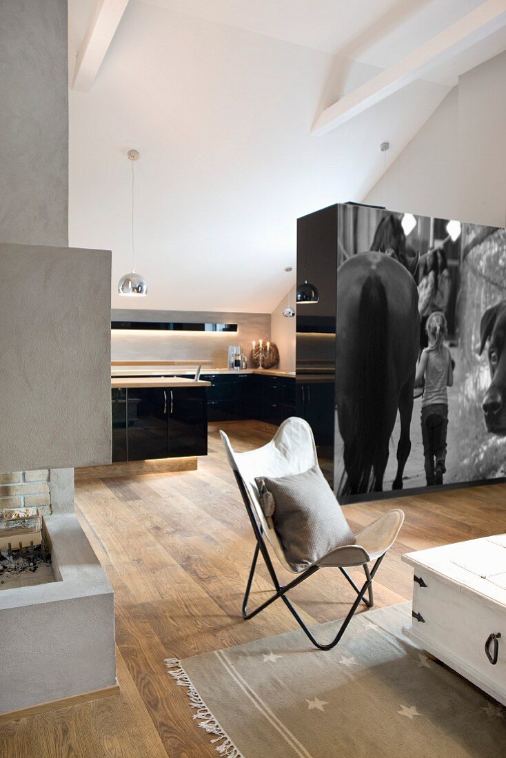 Open-plan interior in bright attic with country-house floorboards and modern, designer fireplace; partition cupboard units with photographic art