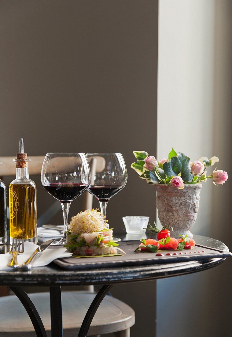 Ceviche, Jakobsmuscheltartar, Rotwein, Olivenöl und Rosenstrauss auf Bistrotisch