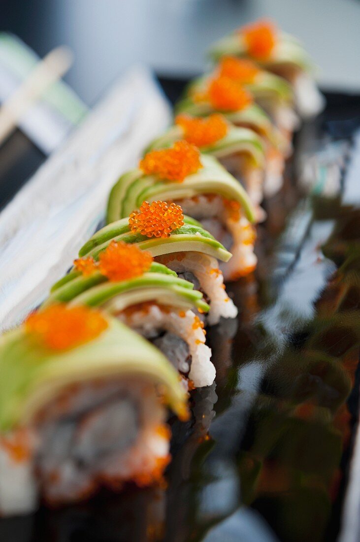 Several pieces of sushi with avocado and caviar, lined up in a row