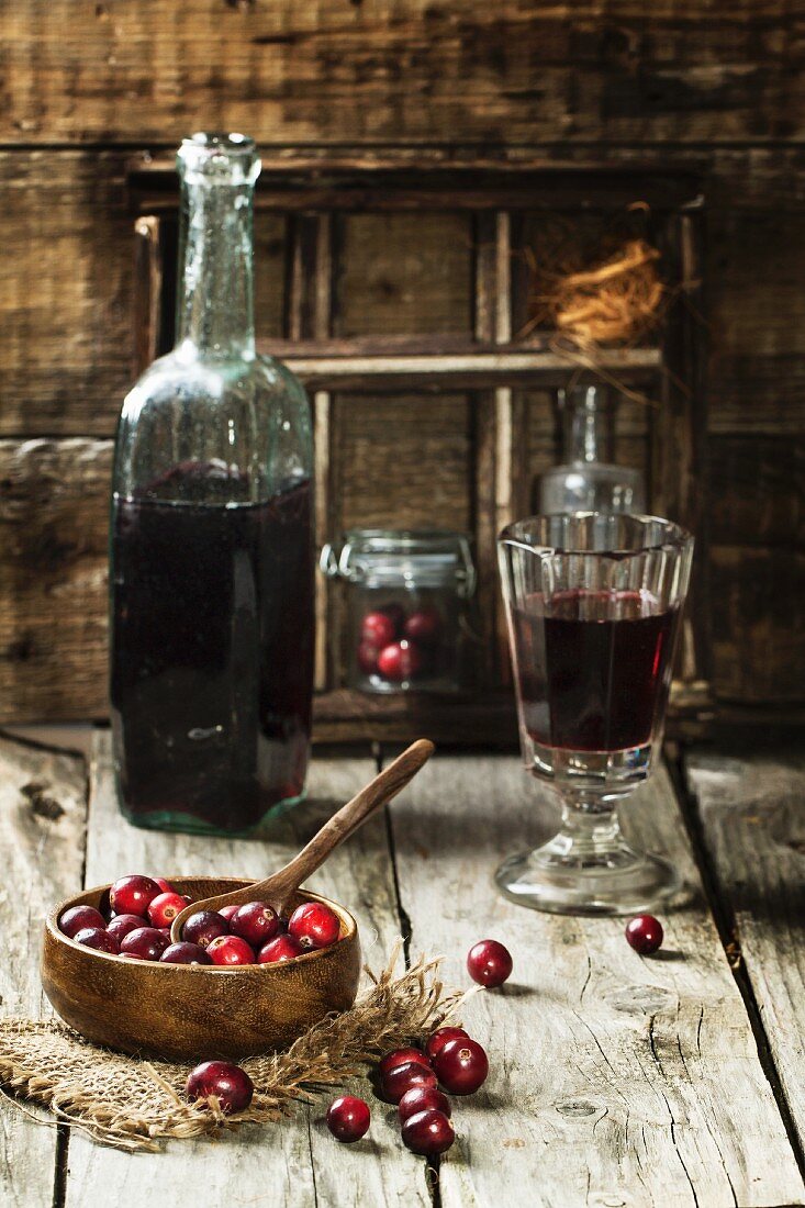 Cranberries in Holzschale und Beerenwein in Glas und Flasche