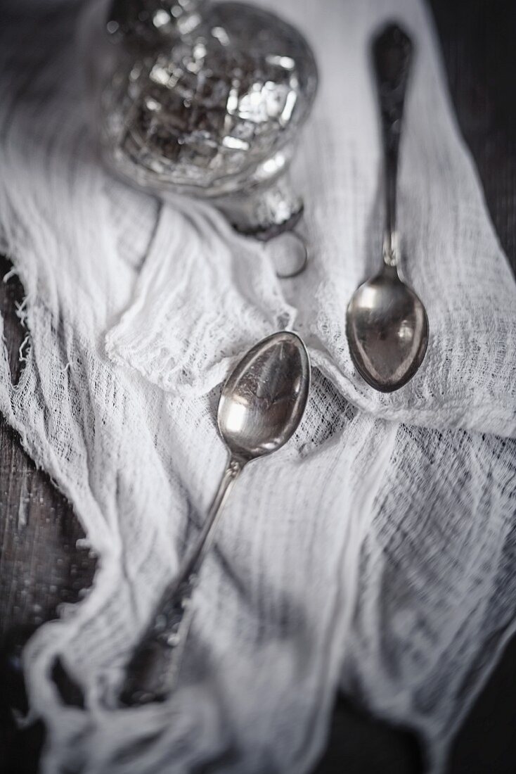 Two teaspoons and a silver Christmas bauble on a muslin cloth