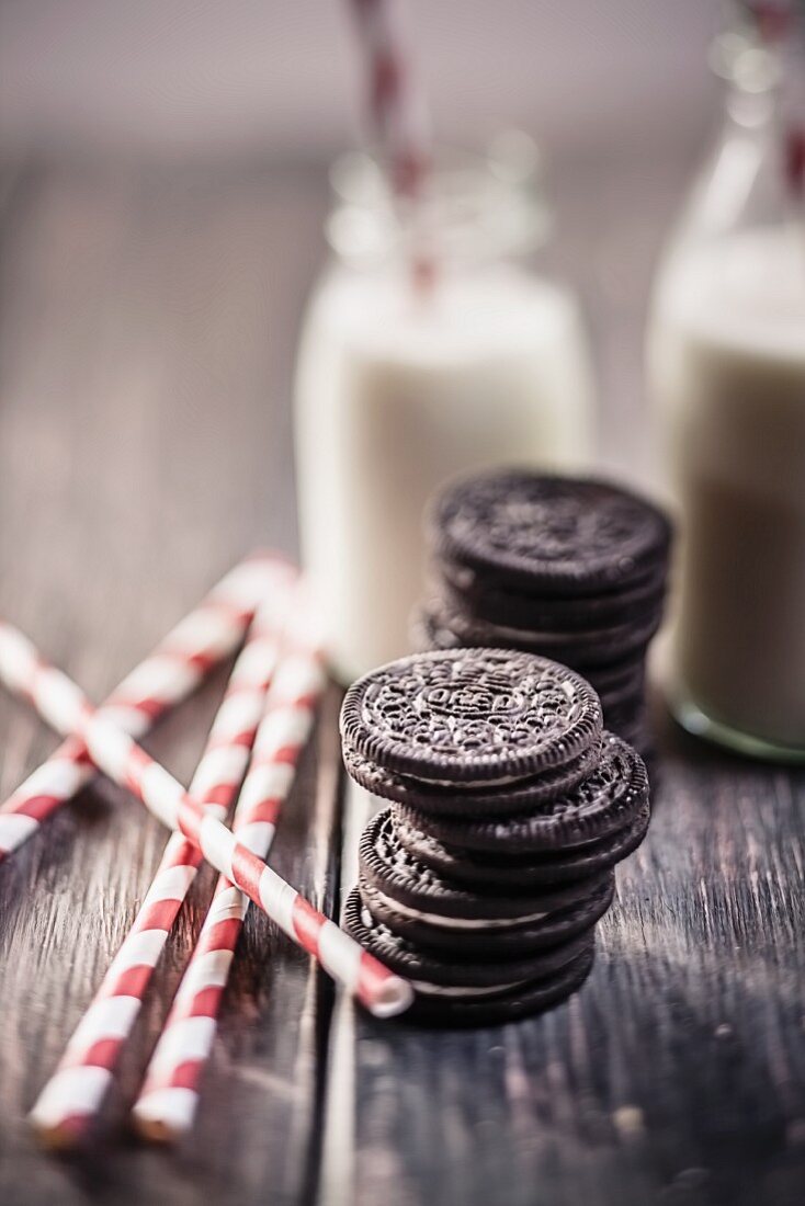 Stacks of Oreo cookies with milk bottles and drinking straws on a wooden slab