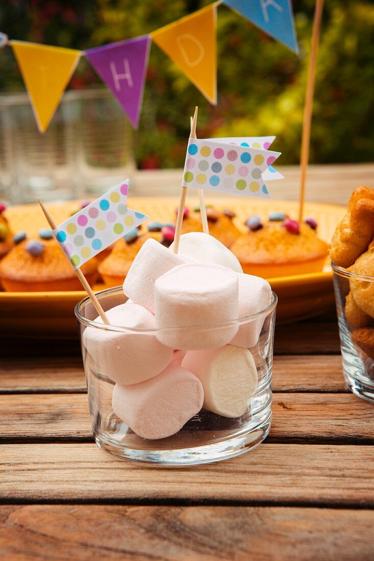 Marshmallows mit Fähnchen dekoriert und Muffins mit Schokolinsen für Kindergeburtstag