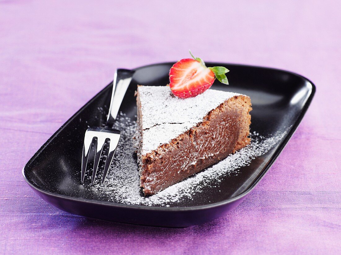 A slice of chocolate torte with icing sugar and a strawberry