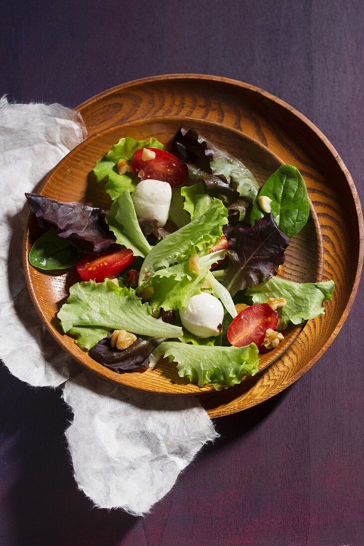 Mixed salad with mozzarella, tomatoes and walnut pieces in a wooden bowl