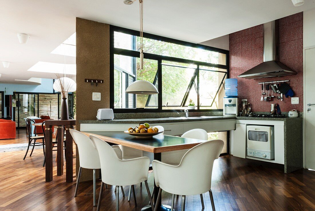 Dining area with sparsely furnished kitchen along two walls in light-flooded, open-plan interior