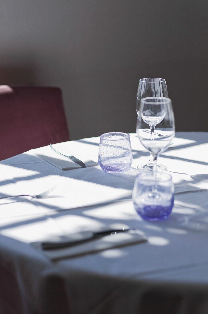 Licht fällt durch ein Fenster auf einen Restauranttisch mit Besteck und Gläsern