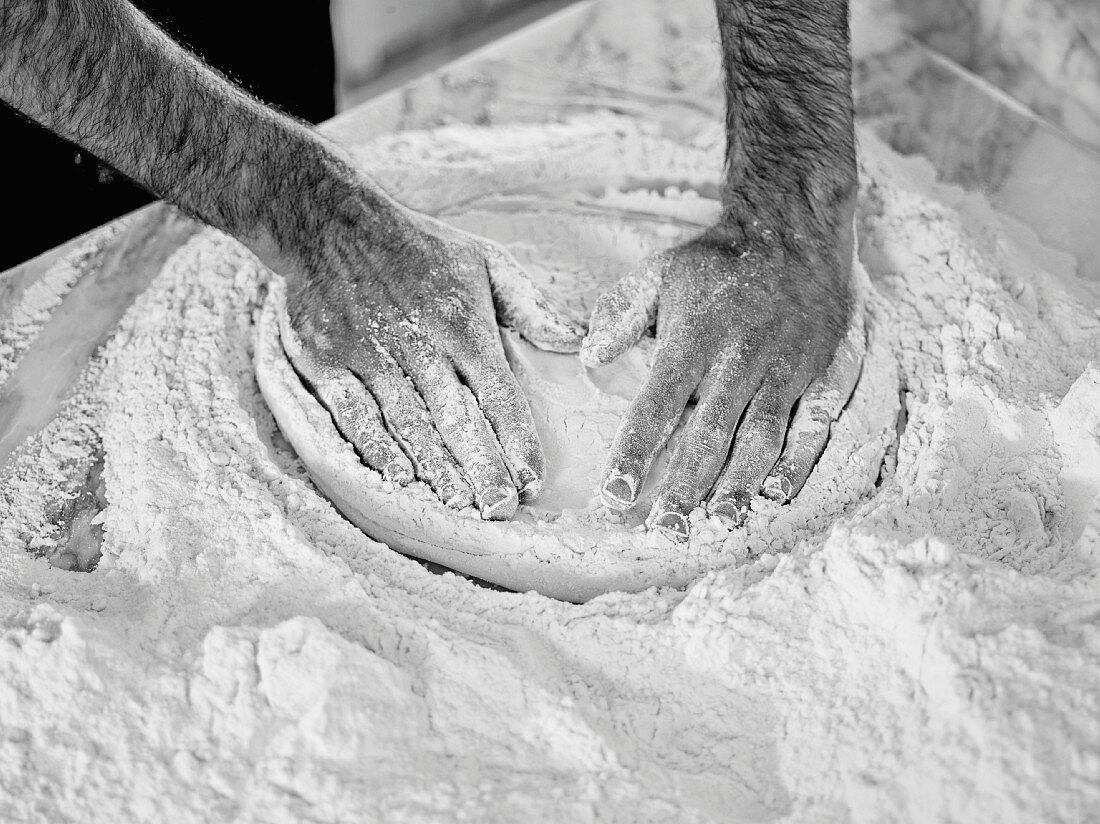 Hands pressing pizza dough flat