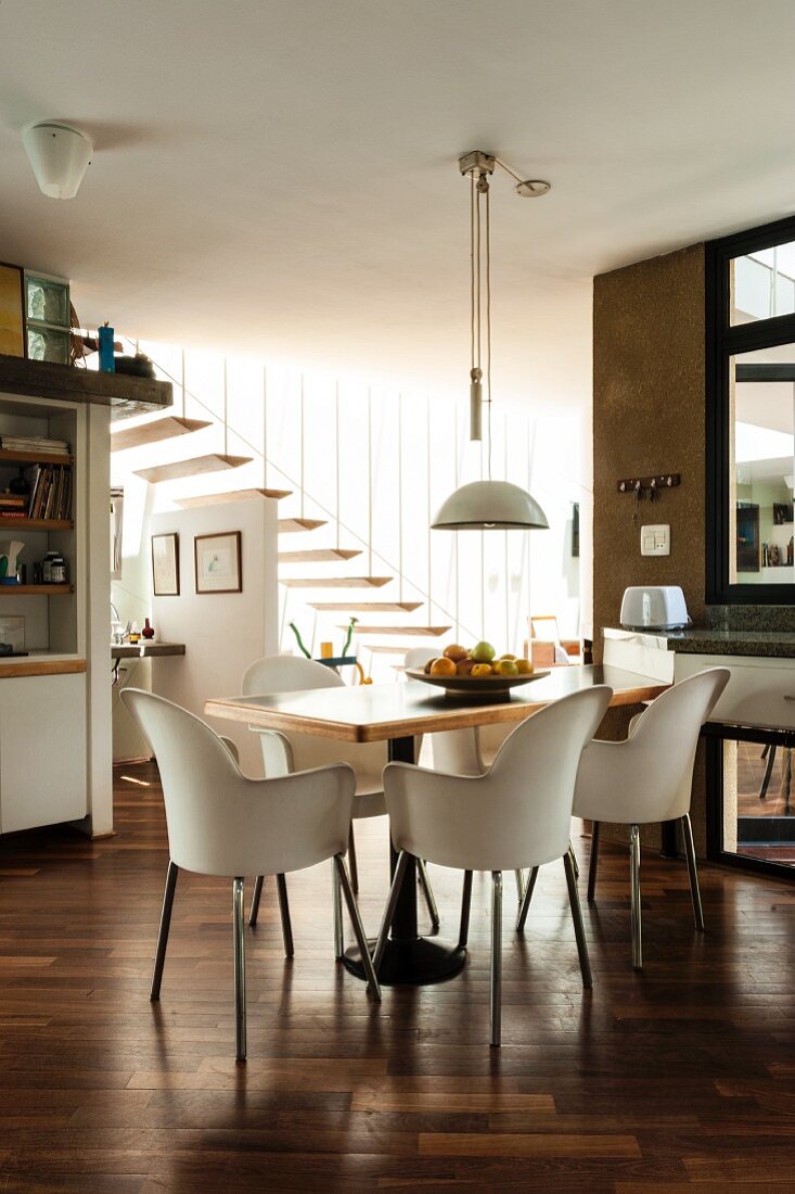 Dining area with shell chairs in open-plan kitchen-dining room; floating stair treads attached to baluster rods in background