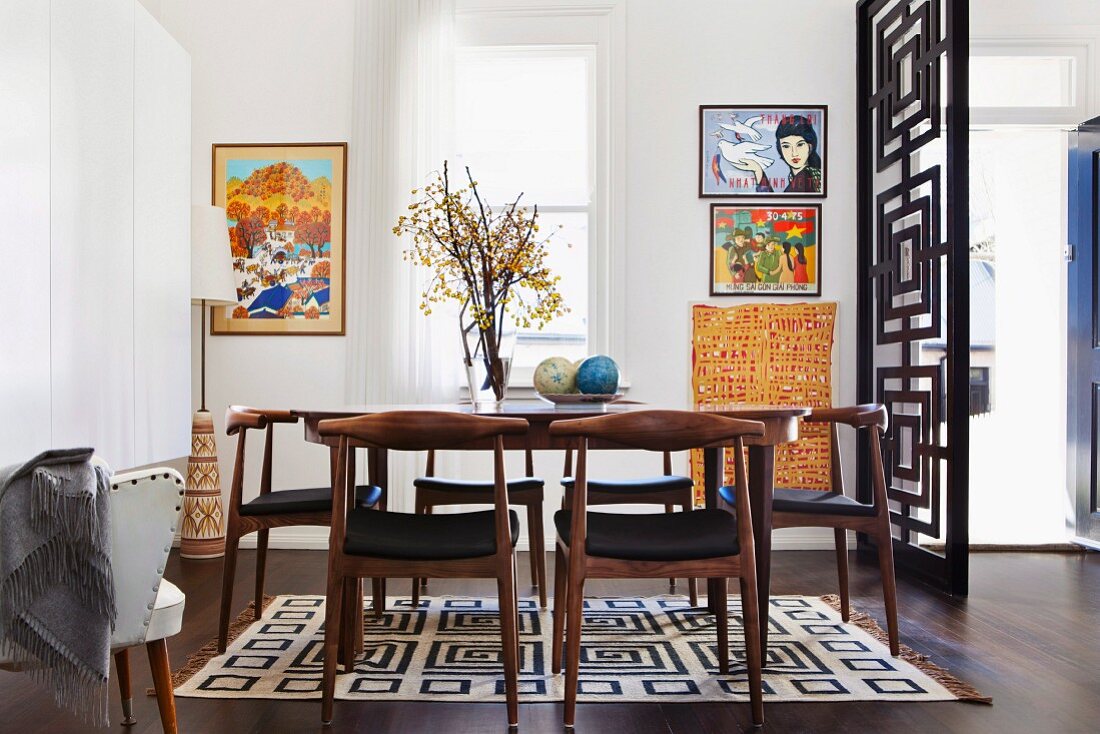 Dining area with classic 50s chairs on geometric rug; open partition wall with concentric square pattern to one side