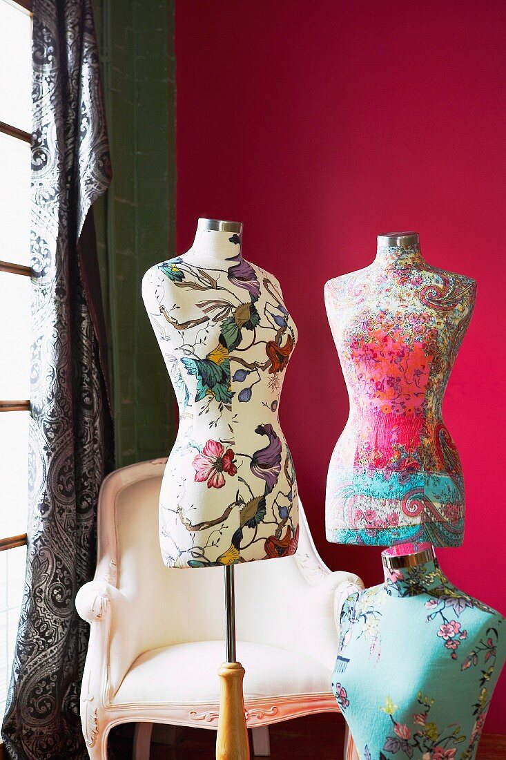 Tailors' dummies covered in floral fabrics against deep pink background