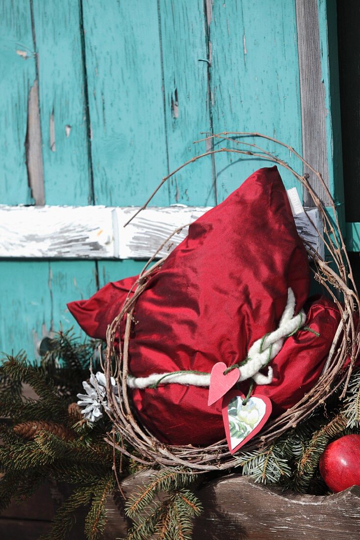 Red silk cushion with vintage Christmas decoration in front of turquoise cabin window shutter