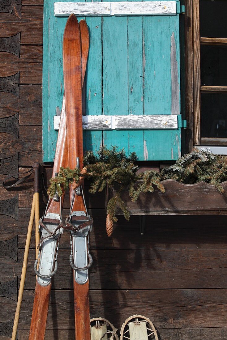 Vintage skis leaning against facade of cabin with turquoise window shutter
