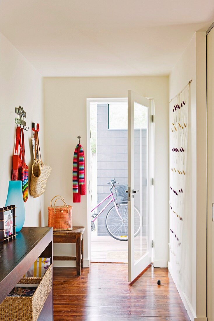 Colourful bags and scarves on wall in bright hallway with open glass door