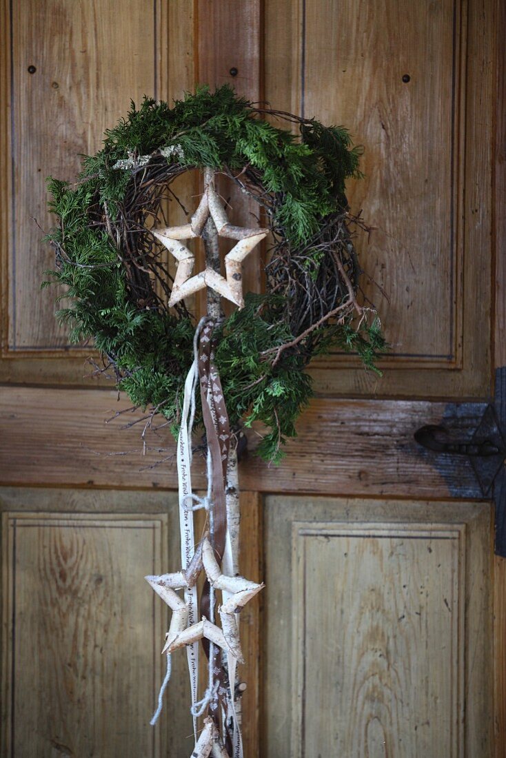 Wreath of Thuja twigs with birch bark star in centre and ribbons hung on rustic wooden door