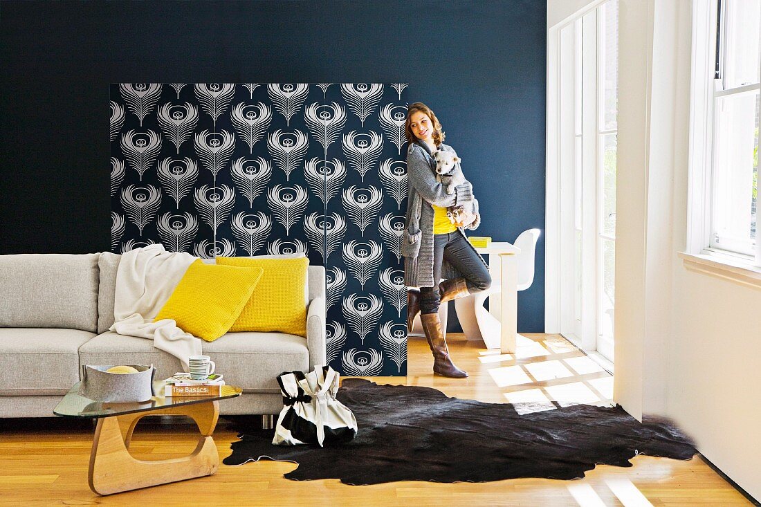 Seating area with sofa, animal-skin rug & coffee table separated by screen wallpapered in black and white floral pattern