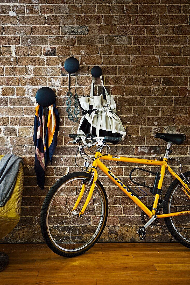 Bicycle leaning on brick wall below decorative black wall hooks for storing bags & utensils