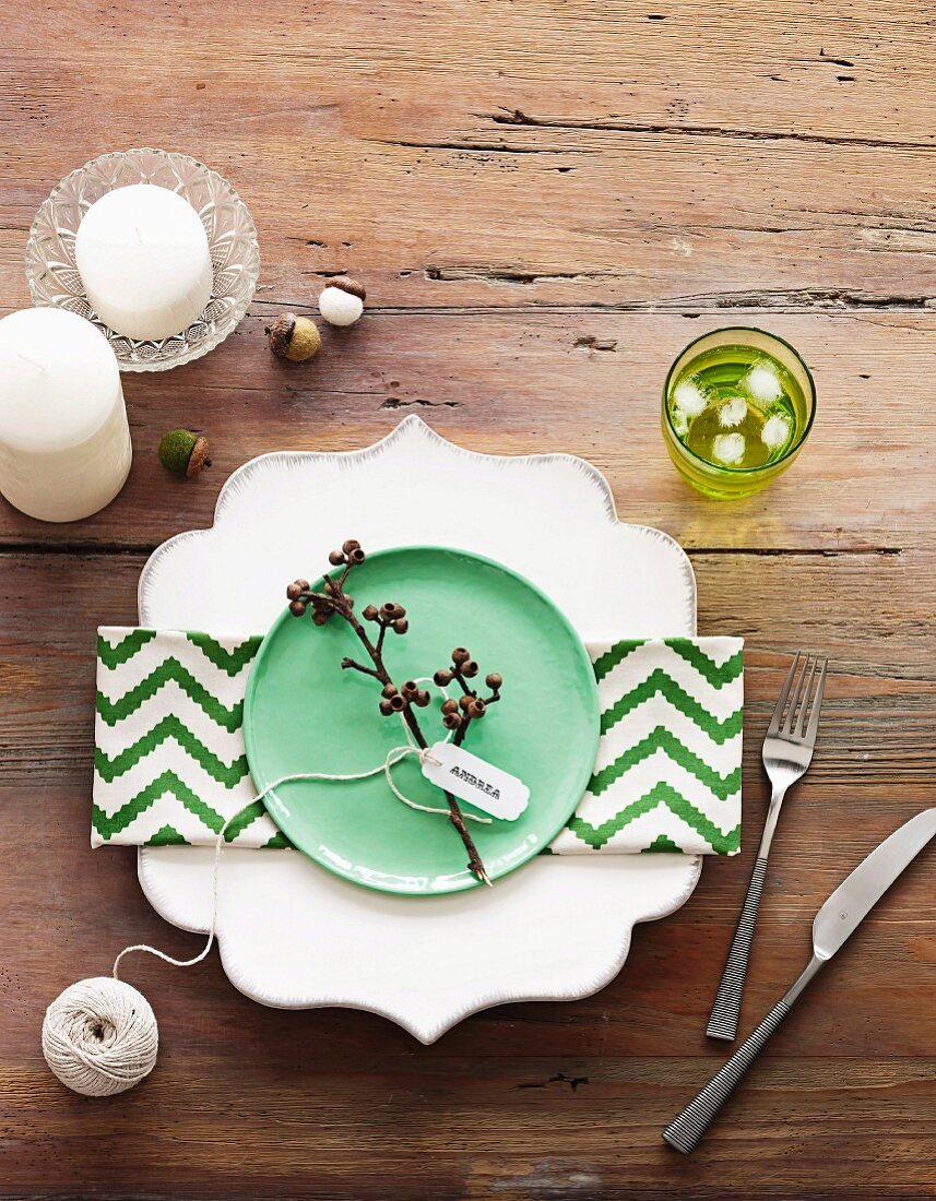 Green and white zig-zag napkin on plate with ornate rim, lime green desert plate and candles arranged on rustic wooden table