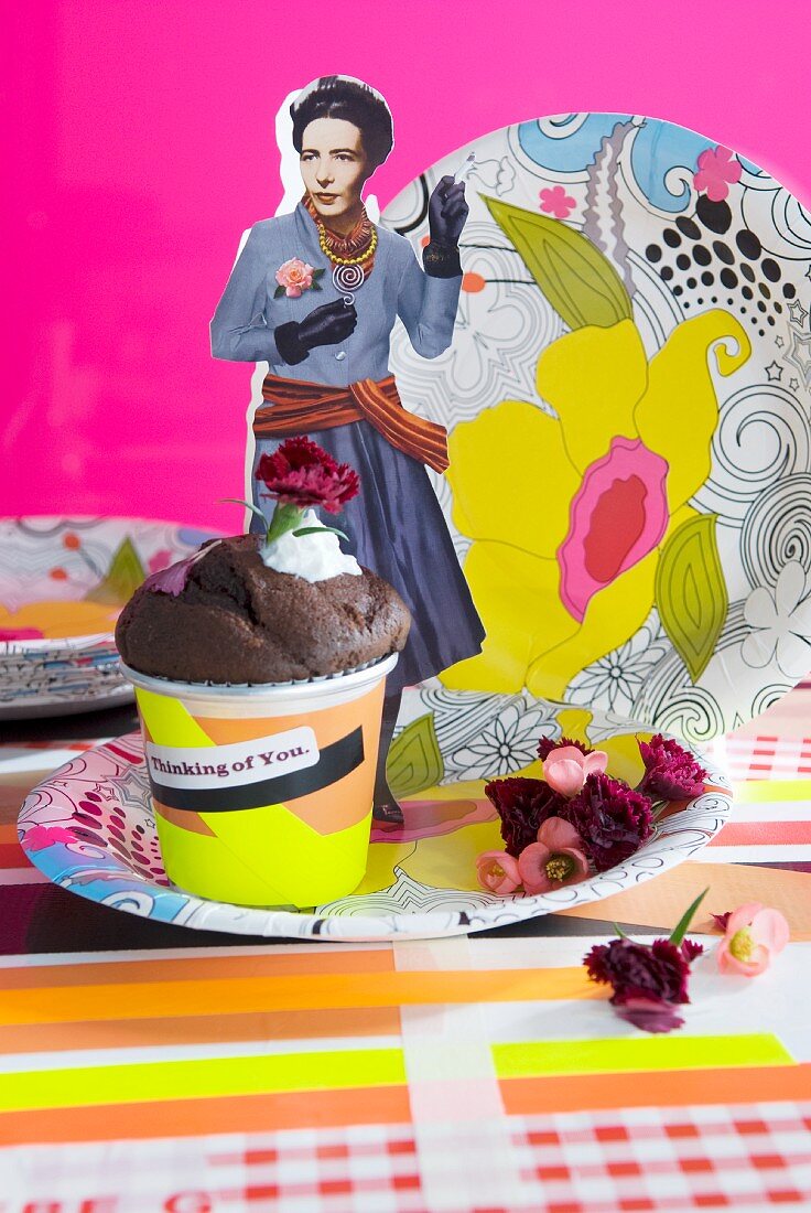 Muffin, colourful paper plates with yellow floral pattern and paper cut-out figurine arranged against pink background